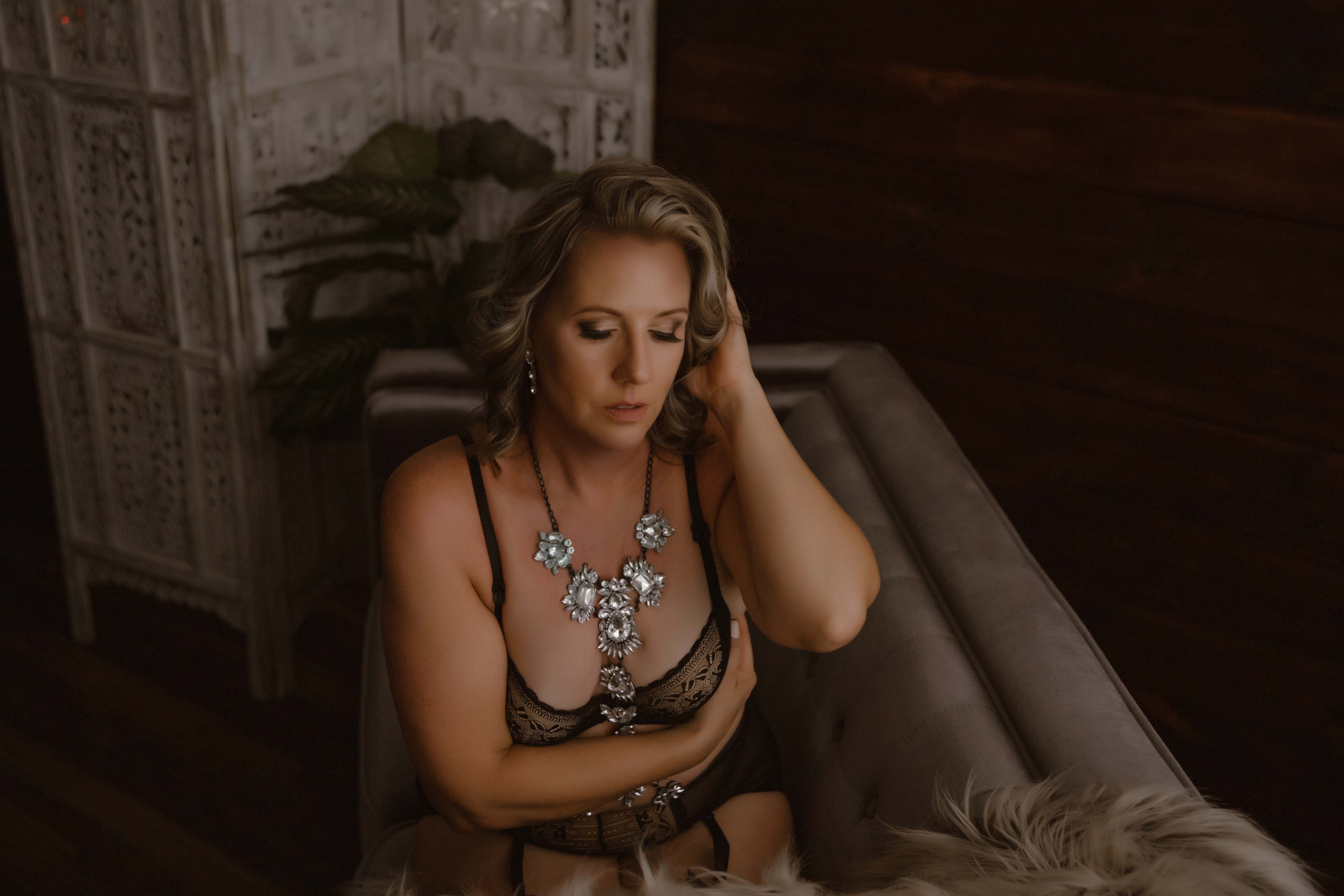 Indoor boudoir photo session of a blonde woman sitting on the couch wearing a black lingerie set