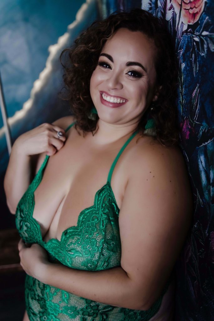 woman wearing green lingerie leaning against a flowered wall looking at the camera